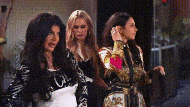three women are standing next to each other in a room and one of them is adjusting her hair .