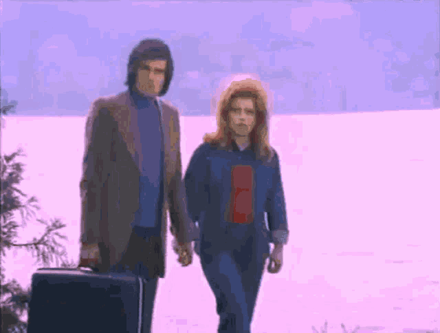 a man and a woman are walking in the snow with a suitcase