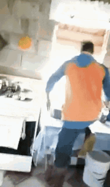 a man in an orange and blue shirt is standing in front of a stove