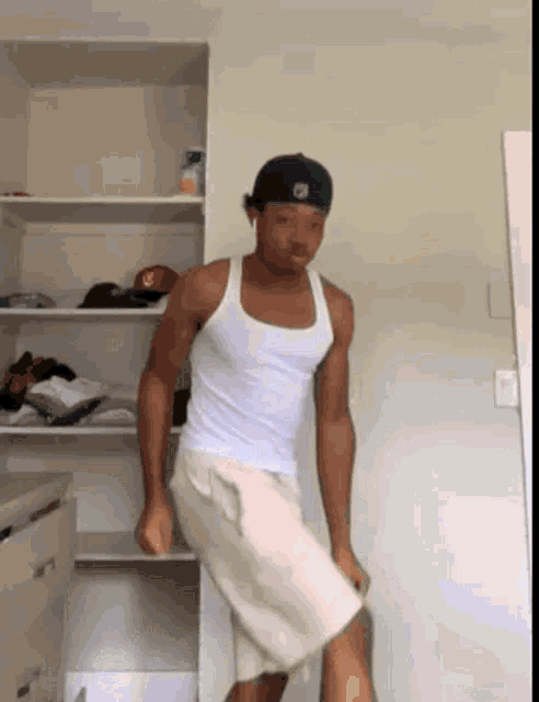 a man wearing a white tank top and shorts is standing in front of a closet