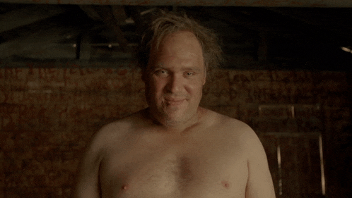 a man without a shirt is smiling in front of a wall that has graffiti on it