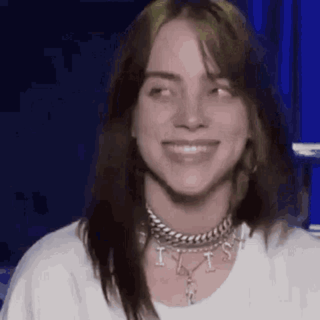 billie eilish is wearing a white shirt and a necklace while smiling .