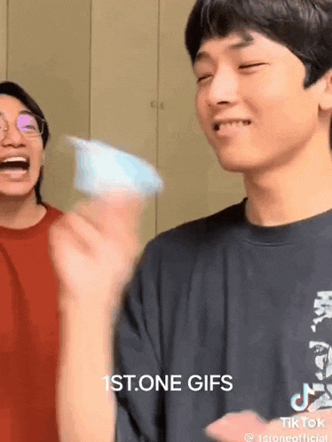 a man in a black shirt is holding a blue object in his hand while a woman laughs behind him .