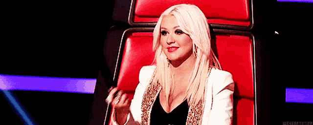 christina aguilera is sitting in a red chair on the voice .