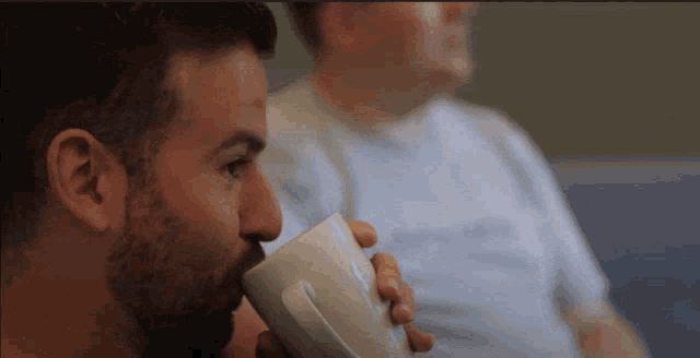 a man with a beard drinking from a white coffee mug