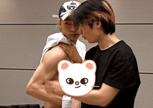 a shirtless man is being held by another shirtless man with a cartoon bear behind him