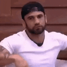 a man with a beard and a hat is wearing a white shirt and a baseball cap .