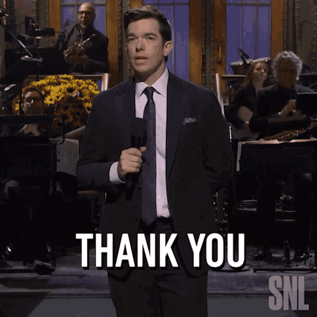 a man in a suit and tie holds a microphone and says " thank you "