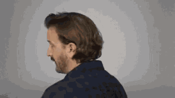 a man with long hair and a beard is looking over his shoulder .