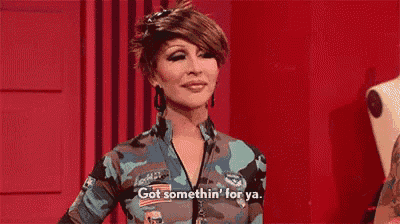 a woman in a camouflage outfit is standing in front of a red wall and talking .