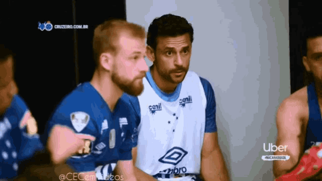 a group of soccer players are sitting in a locker room with uber in the background