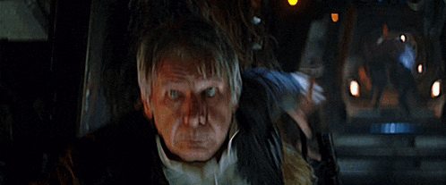 a man in a leather jacket is standing in a dark room with his hands on his head .