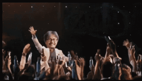 a man is standing on a stage with his arms in the air in front of a crowd .