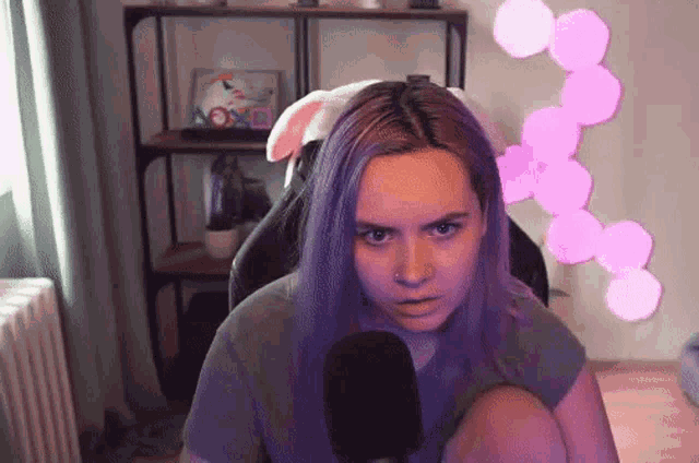 a girl with purple hair is sitting in front of a microphone and looking at the camera .