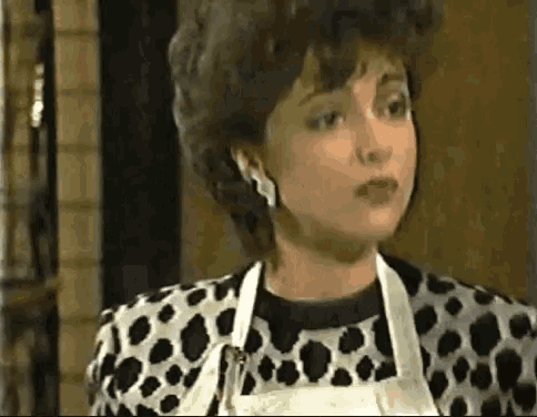 a woman in a dalmatian print jacket and apron is looking at the camera .