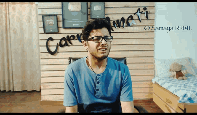 a man wearing glasses and a blue shirt is sitting in front of a wall that says " care amiti "