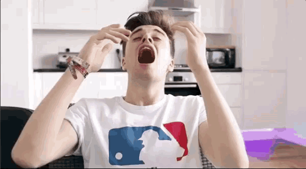 a young man wearing a white t-shirt with a mlb logo on it yawning