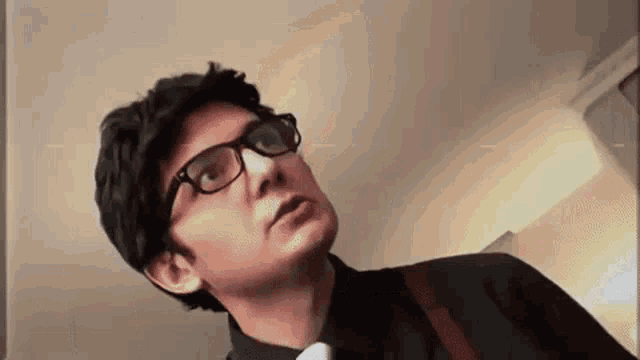 a man wearing glasses and a black shirt and tie is looking up .