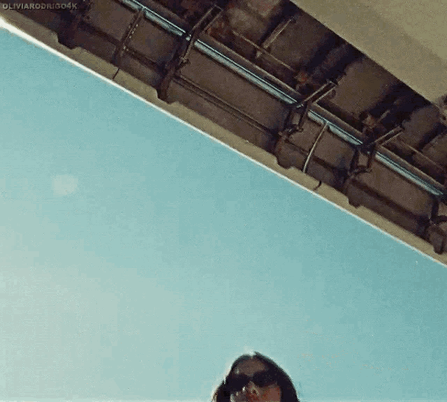a woman wearing sunglasses is standing under a bridge with a blue sky behind her .
