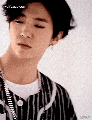 a young man wearing a striped shirt and earrings is looking down .