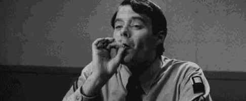 a man is sitting at a table smoking a cigarette .