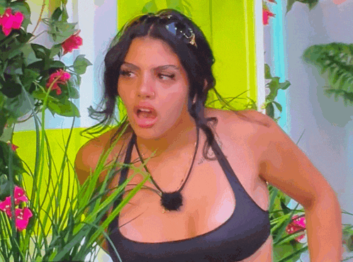 a woman in a black bikini top is standing in a garden with flowers