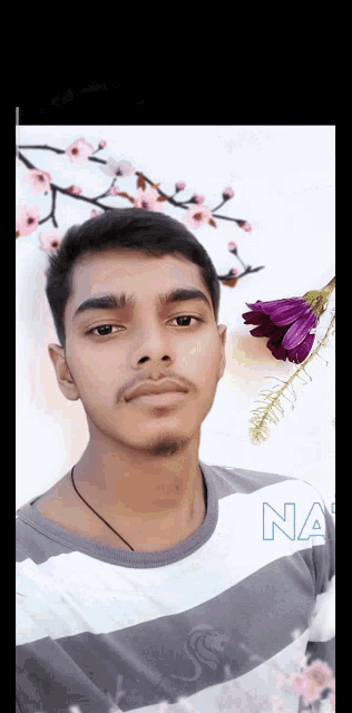 a young man stands in front of a wall with flowers and the word na on the bottom