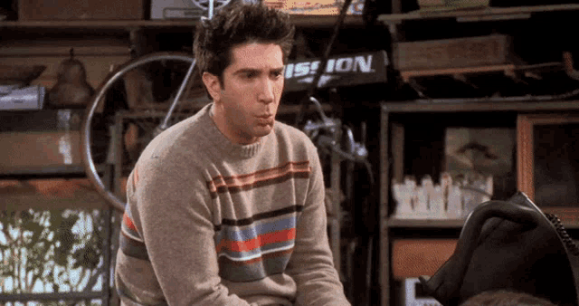 a man wearing a striped sweater is sitting in a garage with a bicycle in the background .