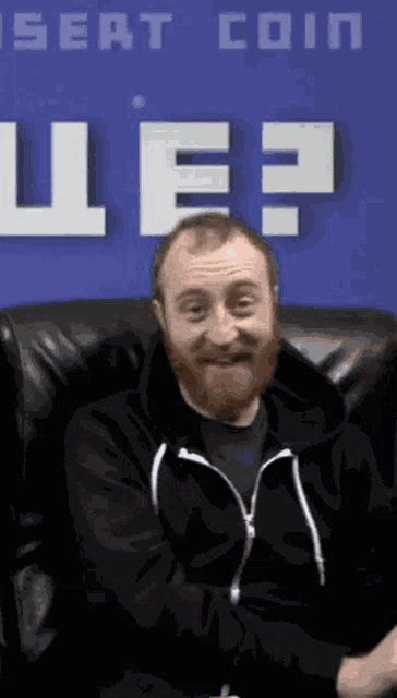 a man with a beard is sitting in front of a sign that says " seat coin "