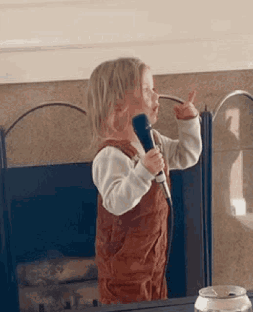 a little girl is singing into a microphone while standing in front of a fireplace .
