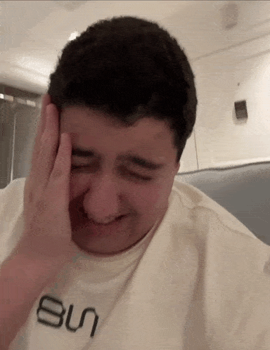 a man wearing a white shirt with the word sun on it is crying .