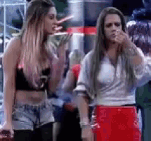 two women are standing next to each other and talking . one of the women is wearing a red skirt .