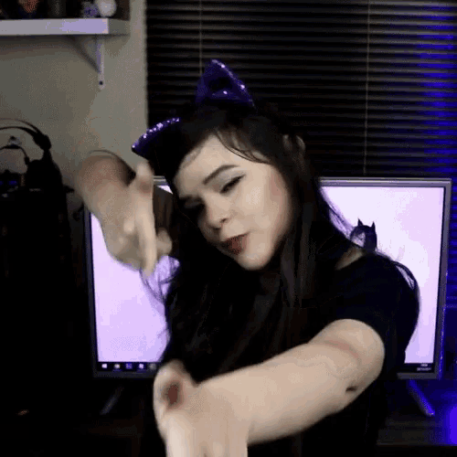 a woman wearing a purple cat ear headband is dancing in front of a computer screen .