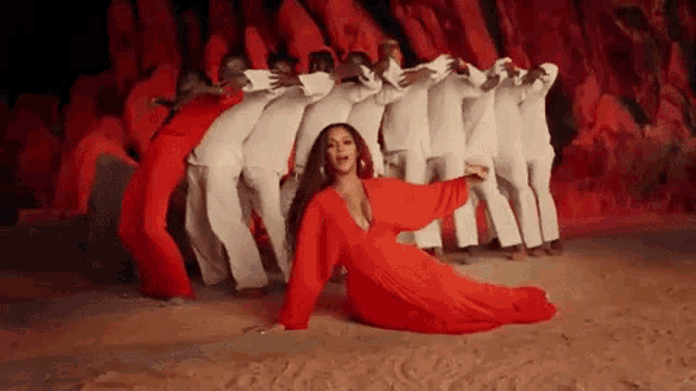 a woman in a red dress is kneeling down in front of a group of dancers in white clothes .