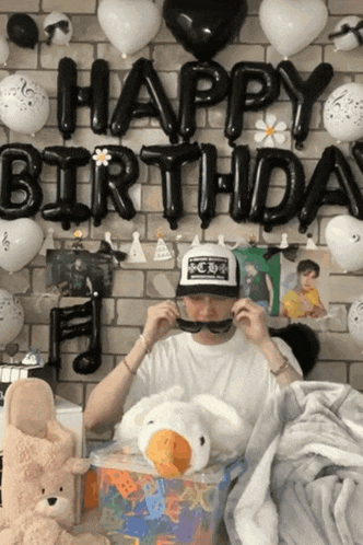 a man sitting in front of a wall with balloons and a sign that says happy birthday