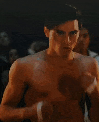 a shirtless man with a bandage on his wrist is standing in a dark room with other men .