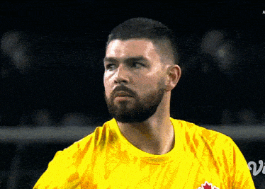 a man with a beard is wearing a yellow shirt that says ' canadian ' on it