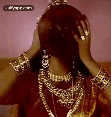 a woman in a red dress and gold jewelry is covering her face with a crown .