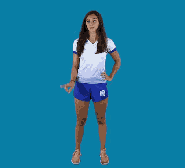 a woman wearing a white shirt and blue shorts with a shield on the shorts