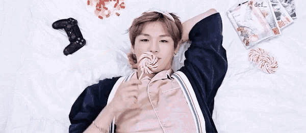 a young man is laying on a bed holding a lollipop in his mouth .
