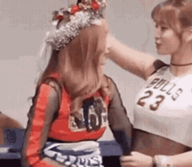 two women are standing next to each other and one is putting a crown on the other 's head .