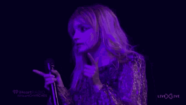 a woman is singing into a microphone on a stage in a dark room .