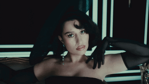 a woman in a black dress and black gloves is looking down