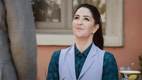 a woman in a blue shirt and a gray vest is standing in front of a building .