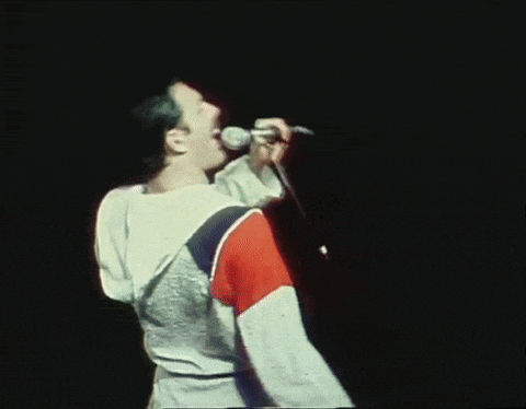 a man singing into a microphone with his arms outstretched in the dark