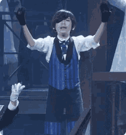 a boy in a blue vest and bow tie is standing on a stage with his arms outstretched .