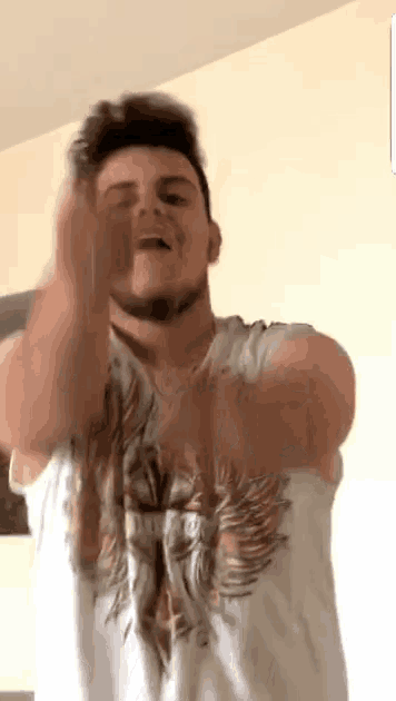 a man in a white t-shirt is making a funny face with his hands in the air .