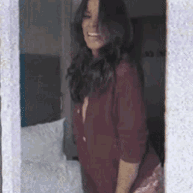 a woman in a red shirt is standing in front of a window in a bedroom .