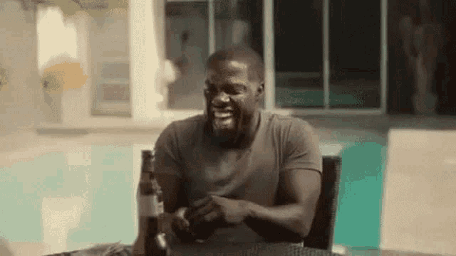 a man is sitting at a table with a bottle of beer and laughing .