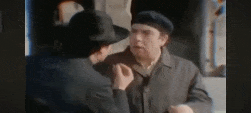 a man in a hat is talking to another man in a suit and coat .